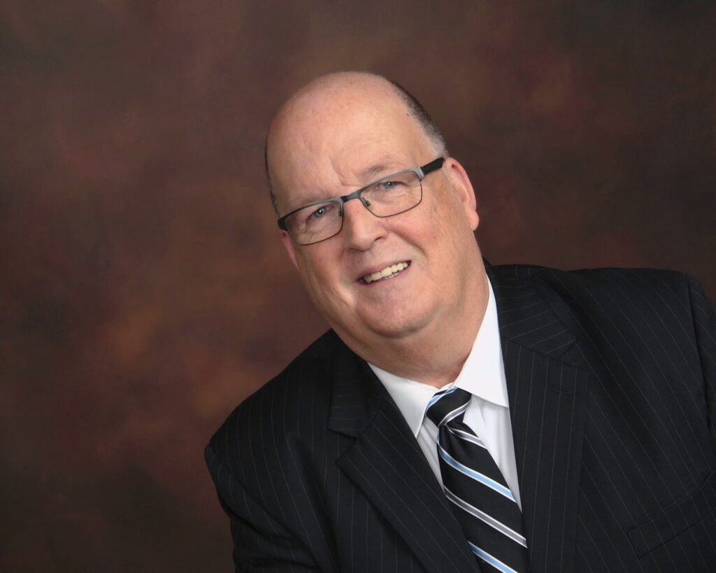 Man in suit with glasses, smiling warmly.
